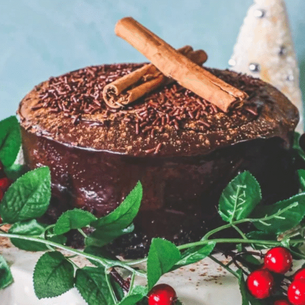 A Chocolate Chinese Five Spice Cake topped with cocoa powder, chocolate sprinkles, and two cinnamon sticks, decorated with green leaves and red berries.