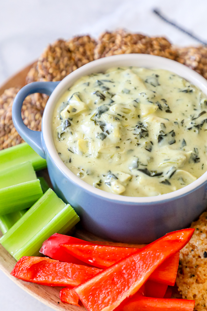 spinach dip in a center bowl with crackers, peppers, and celery around it