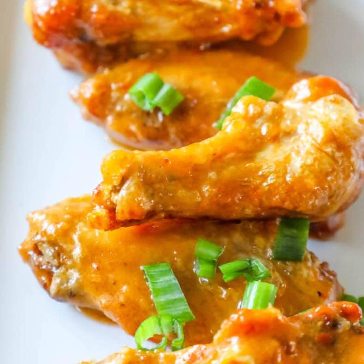 chicken wings in sauce on a plate with chopped scallions