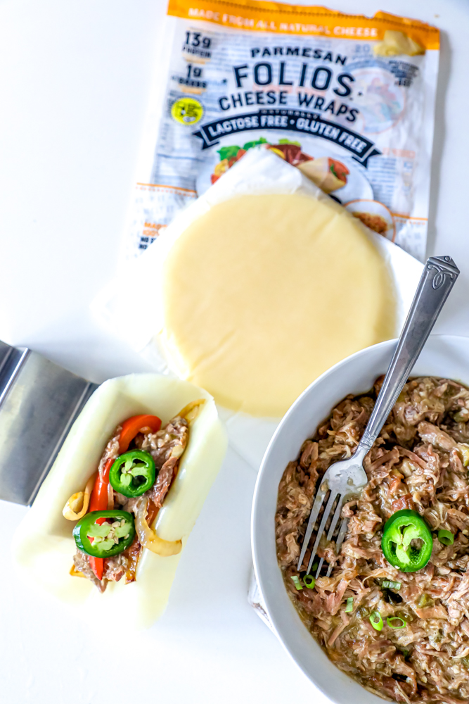 A bowl of Green Chile Pork Carnitas with a fork and a package of cheese wraps.