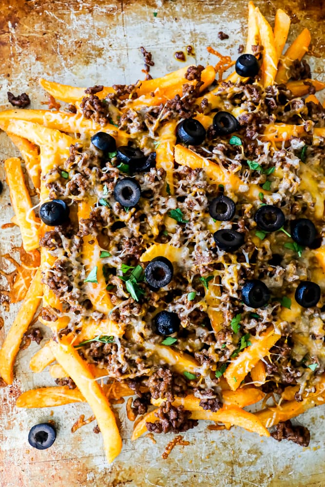 Cheesy nachos with meat and olives baked on a sheet.