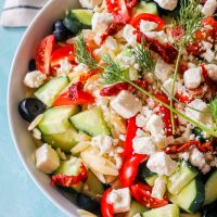 feta, cucumbers, tomatoes, olives, orzo, and dill in a bowl