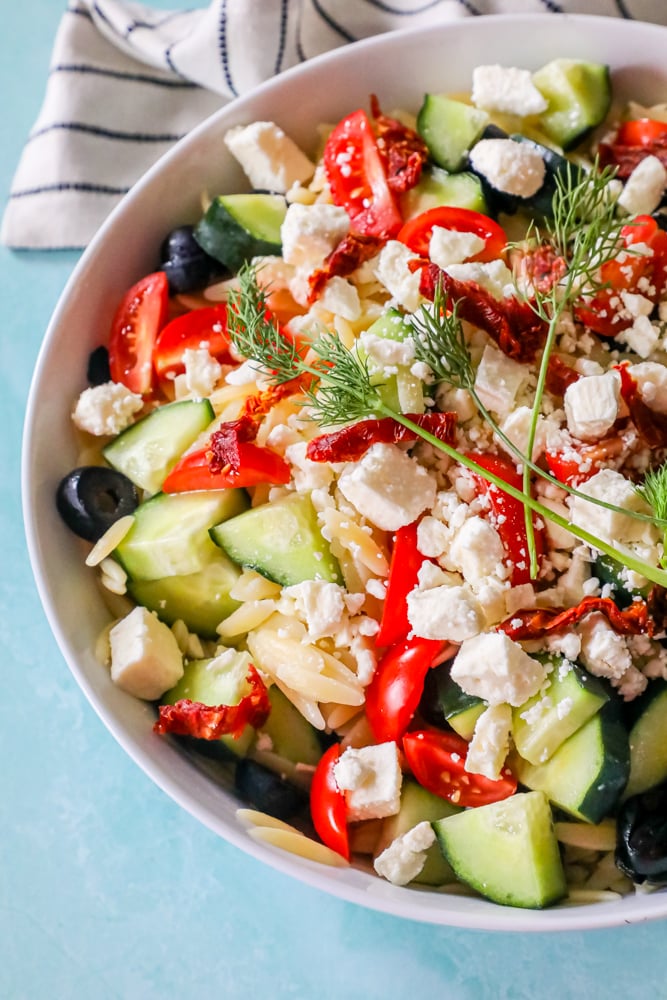 cherry tomatoes, olives, sun dried tomatoes, feta cheese, cucumbers, and fresh dill in a bowl over orzo.