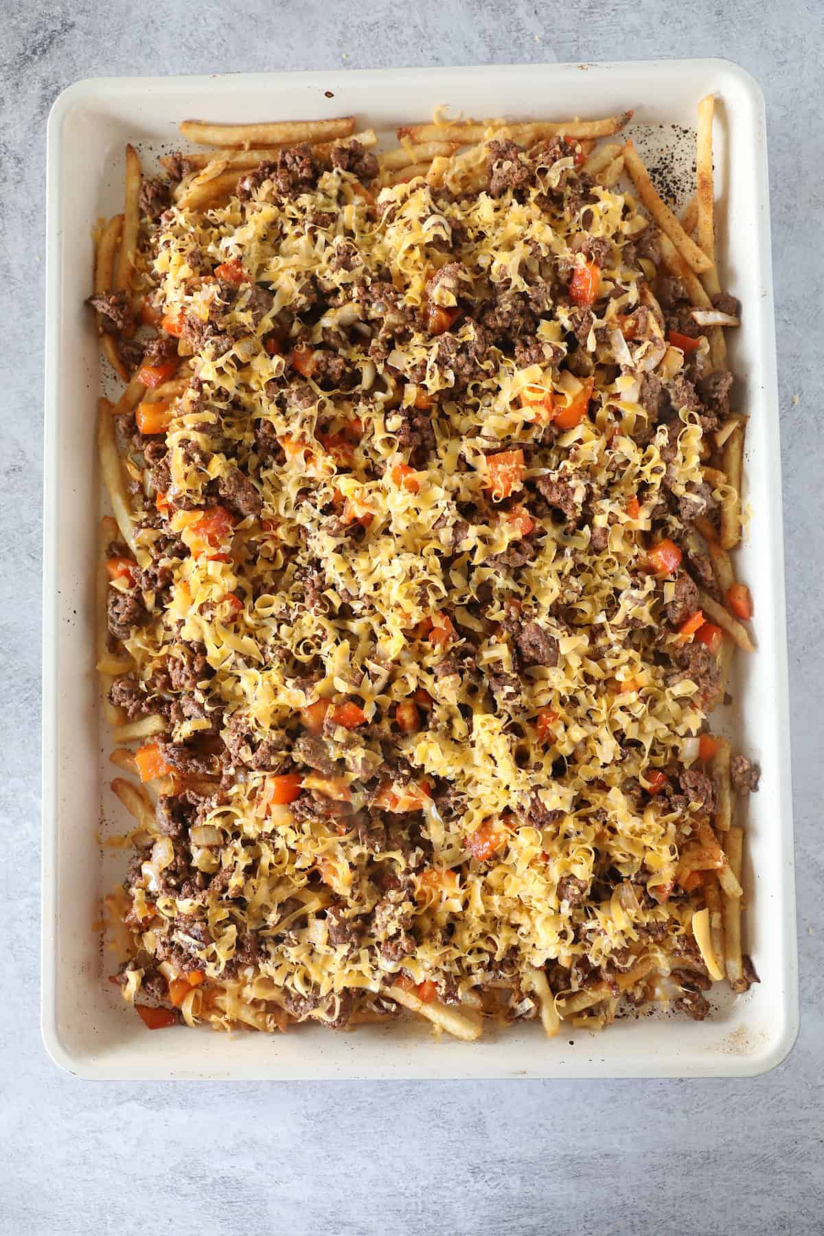 A baking dish filled with a layered casserole made of cooked ground beef, pasta, diced carrots, and melted cheese on top—like an Easy Nacho Fries twist in casserole form.