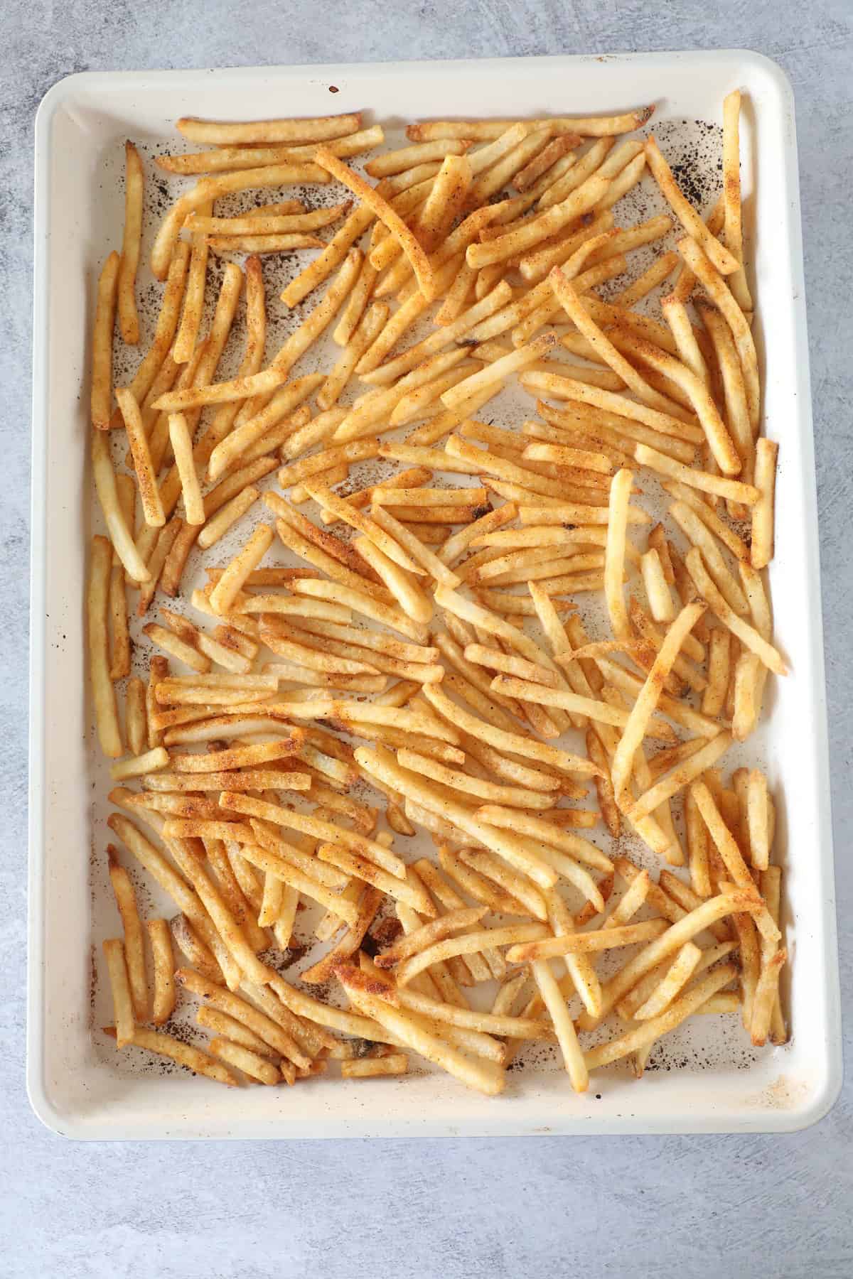 A baking sheet filled with evenly spread, seasoned French fries on a light gray surface—perfect for trying an Easy Nacho Fries twist or your favorite French Fry Nachos recipe.