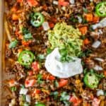 A close-up of Easy Nacho Fries loaded with ground beef, melted cheese, diced tomatoes, onions, jalapeños, guacamole, sour cream, and chopped cilantro.