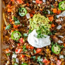A close-up of Easy Nacho Fries loaded with ground beef, melted cheese, diced tomatoes, onions, jalapeños, guacamole, sour cream, and chopped cilantro.