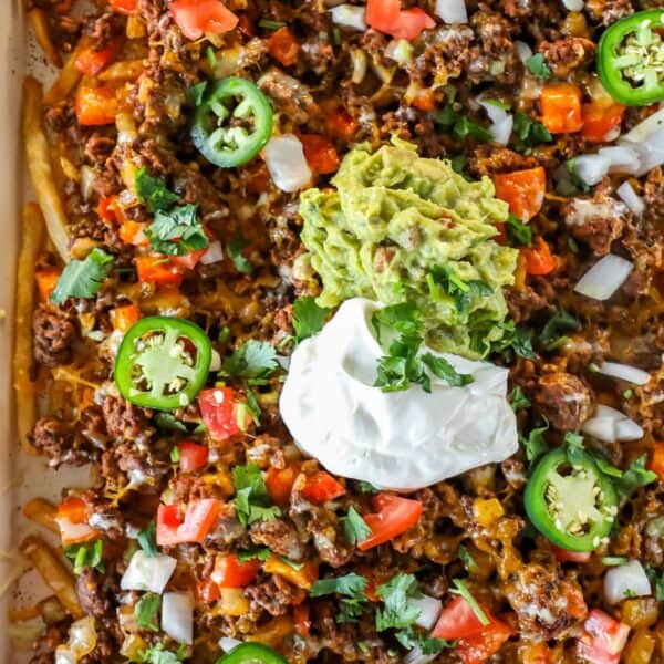 A close-up of Easy Nacho Fries loaded with ground beef, melted cheese, diced tomatoes, onions, jalapeños, guacamole, sour cream, and chopped cilantro.