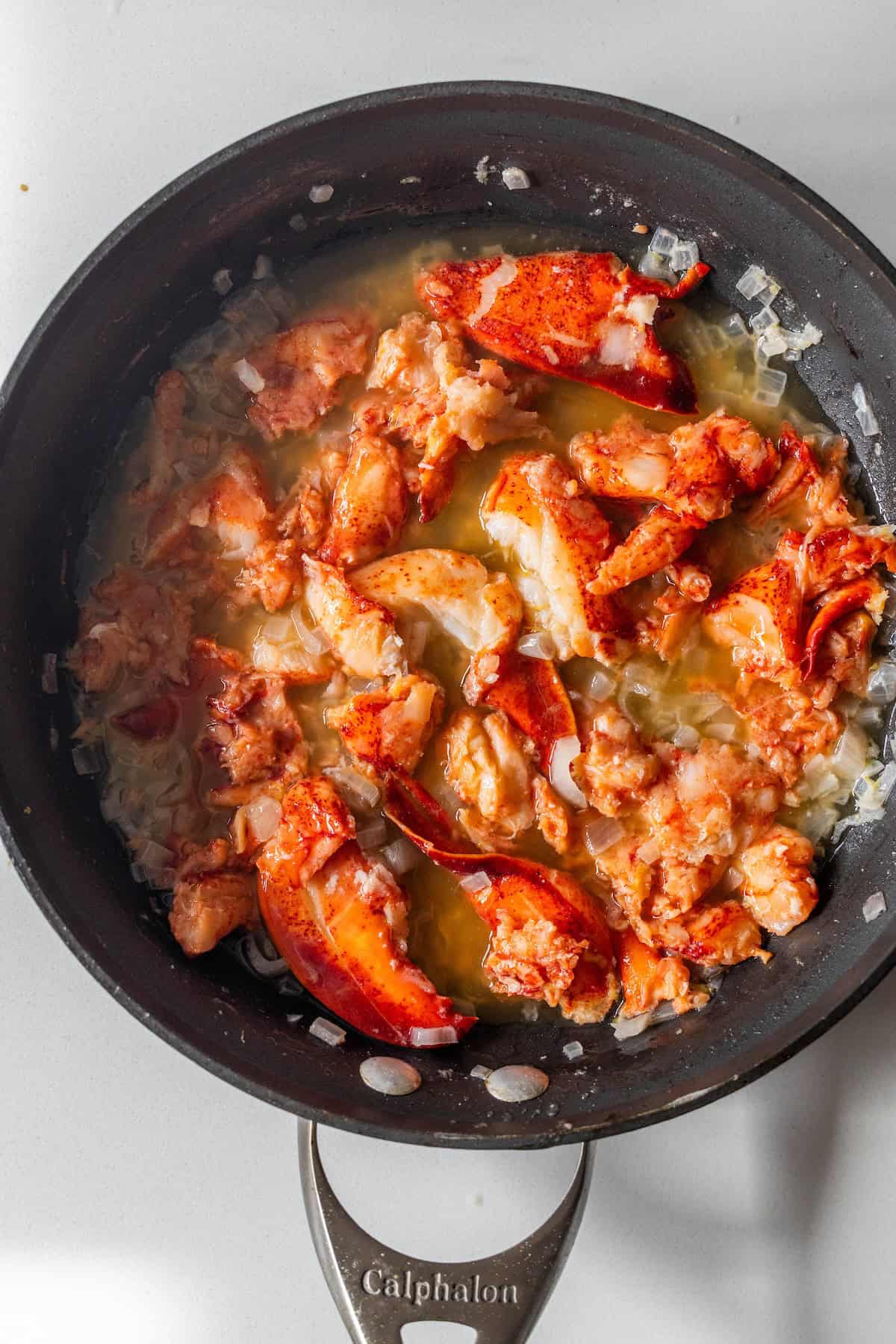 Cooked lobster meat with chopped onions in melted butter, creating an easy garlic butter lobster skillet, served sizzling in a black skillet on a white surface.