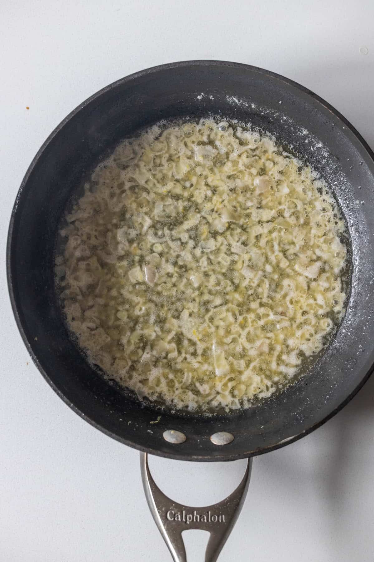 A frying pan on a white surface contains chopped onions sautéing in melted butter—a perfect start for an Easy Garlic Butter Lobster Skillet.