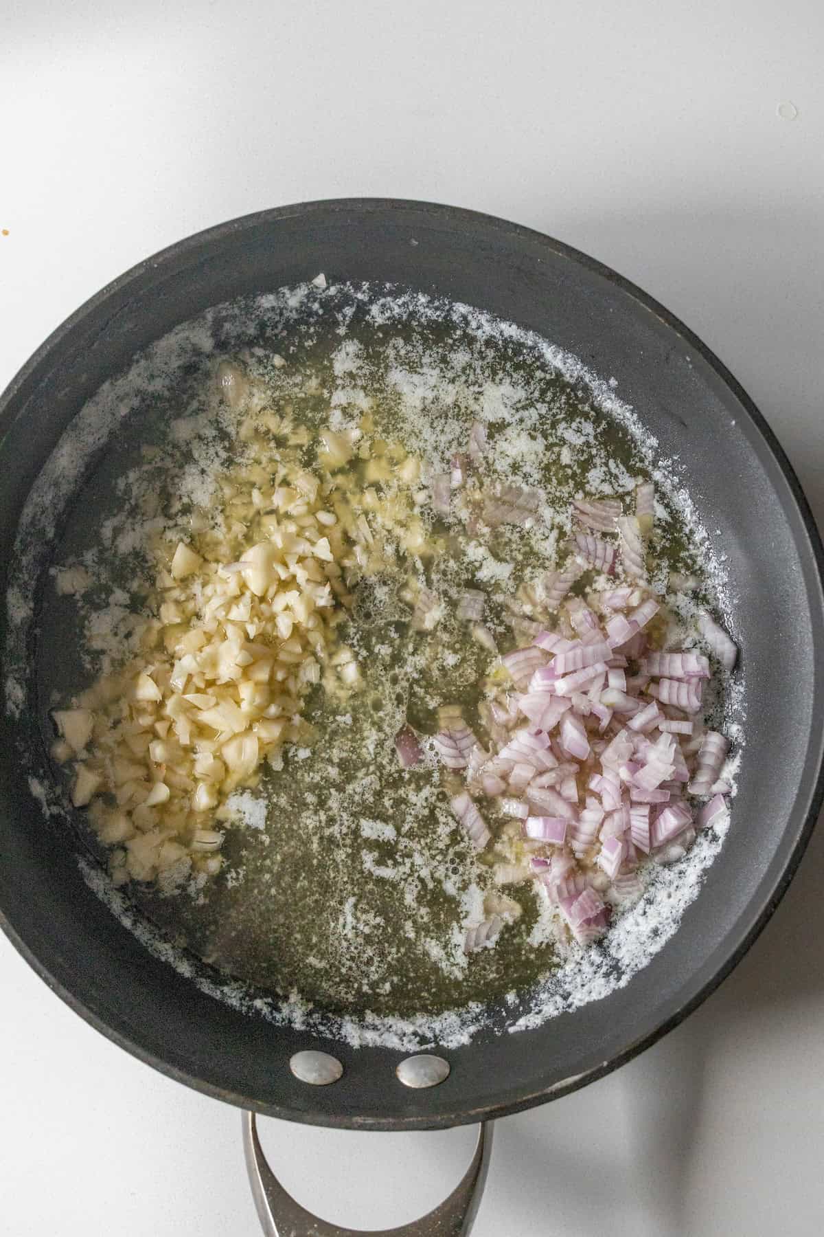 Chopped garlic and diced shallots sautéing in melted butter in a black frying pan, ready to create the perfect Lobster Skillet Dinner.
