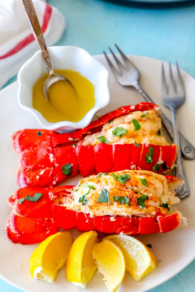 lobster tails seasoned with paprika and butter on a white plate with chopped parsley on top and lemon slices on the side in front of an Instant Pot pressure cooker