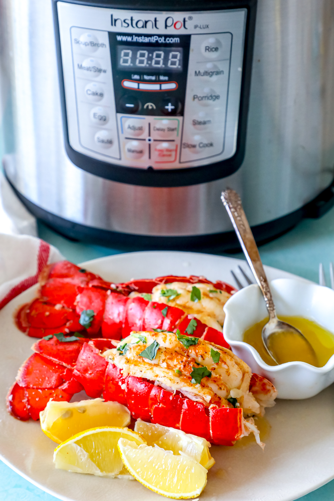 lobster tails seasoned with paprika and butter on a white plate with chopped parsley on top in front of an Instant Pot pressure cooker
