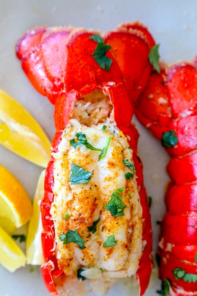 lobster tail seasoned with paprika and butter on a white plate with chopped parsley on top