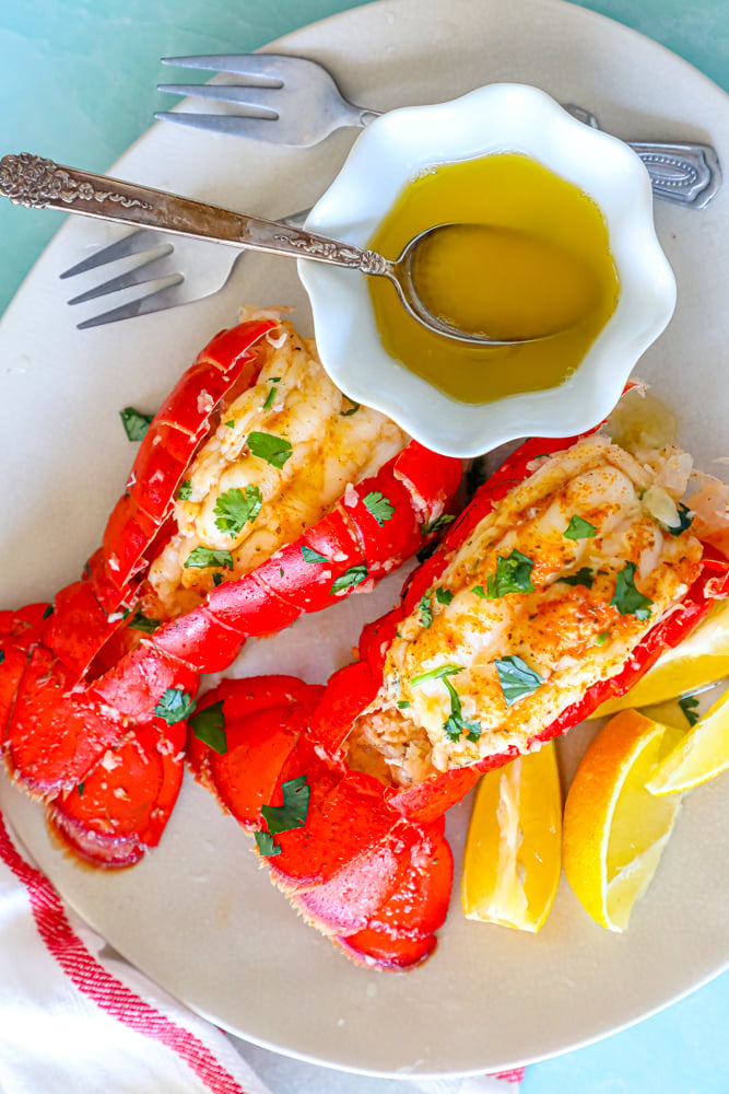 two red lobster tails seasoned with paprika and butter on a white plate with chopped parsley on top