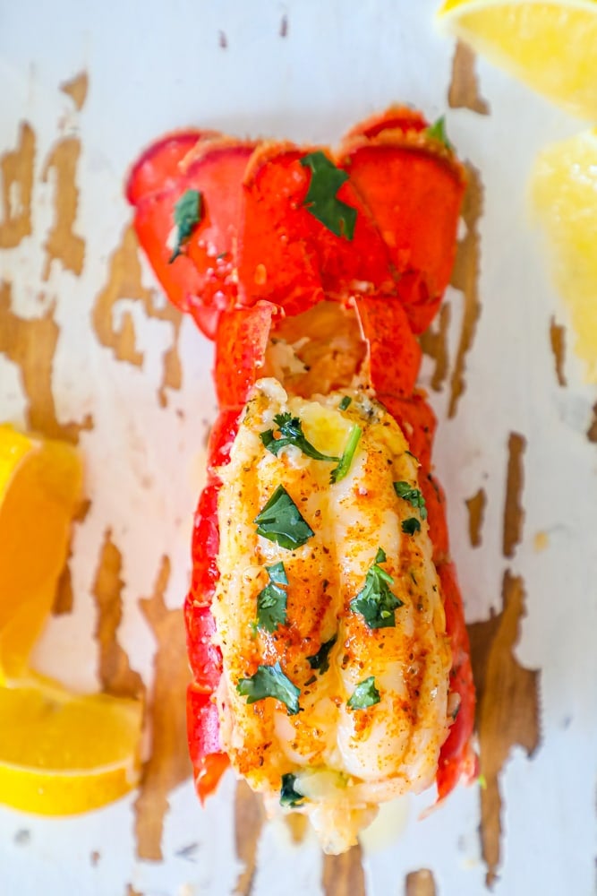 broiled lobster tail with parsley and lemon wedges on a white painted wood board