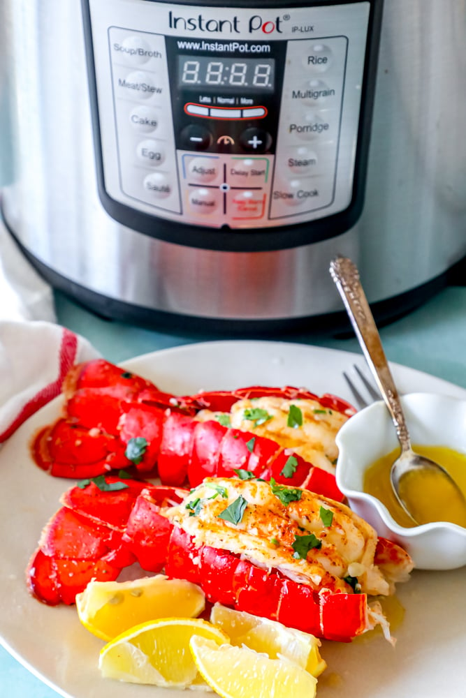 lobster tails seasoned with paprika and butter on a white plate with chopped parsley on top in front of an Instant Pot pressure cooker