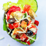 A halved avocado filled with diced chicken, chopped tomatoes, sliced olives, shredded cheese, and a wedge of lime creates a delicious keto chicken taco avocado.