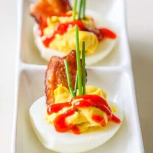 Deviled eggs with bacon and ketchup on a white plate.