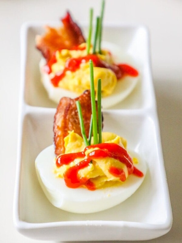 Deviled eggs with bacon and ketchup on a white plate.