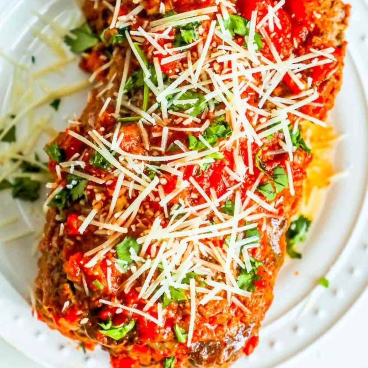 Meatloaf with marinara sauce and parmesan cheese on a white plate, the best easy baked Italian meatloaf recipe ever.