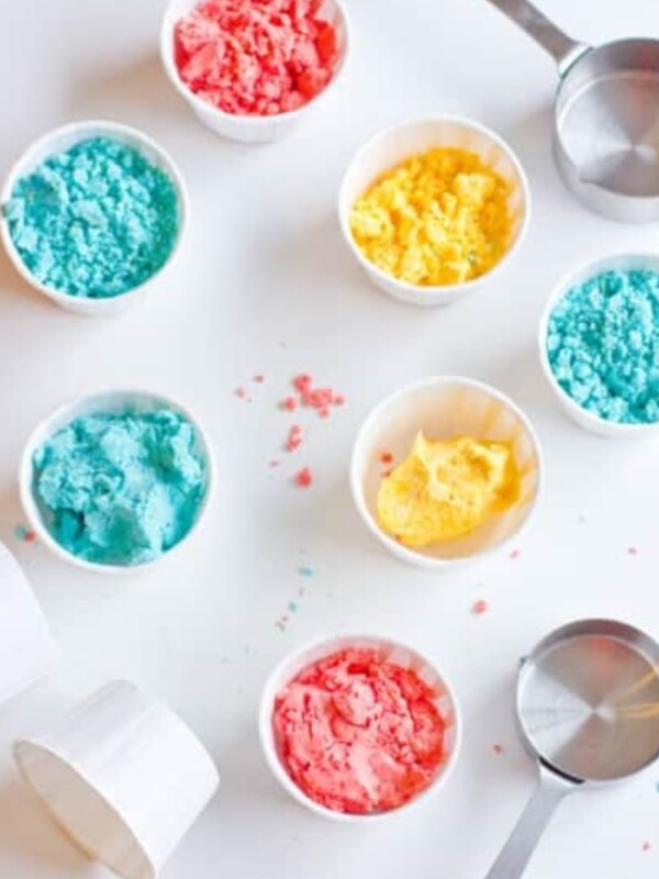 Colorful sprinkles and small bowls on a white surface for making homemade gluten-free moon sand.