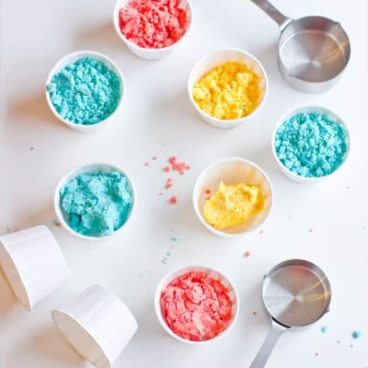 Colorful sprinkles and small bowls on a white surface for making homemade gluten-free moon sand.