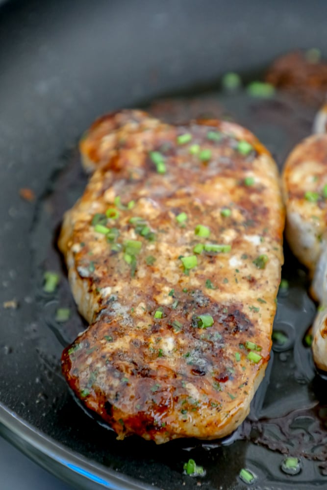 minced chives on top of a pork chop in a black pan 