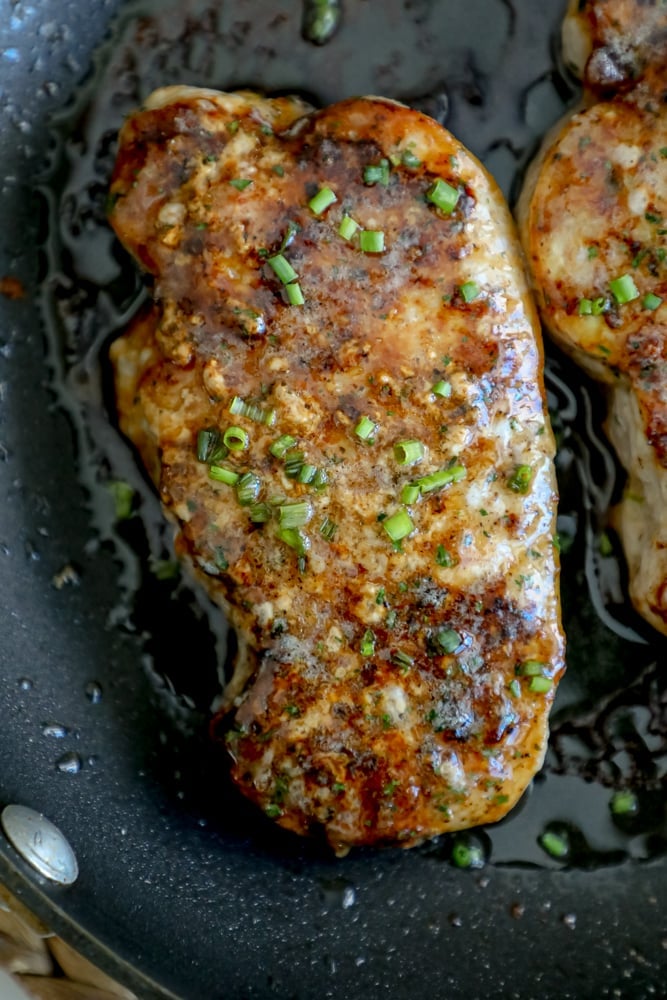 black pan with browned ranch pork chops topped with chives and ranch dressing seasonings