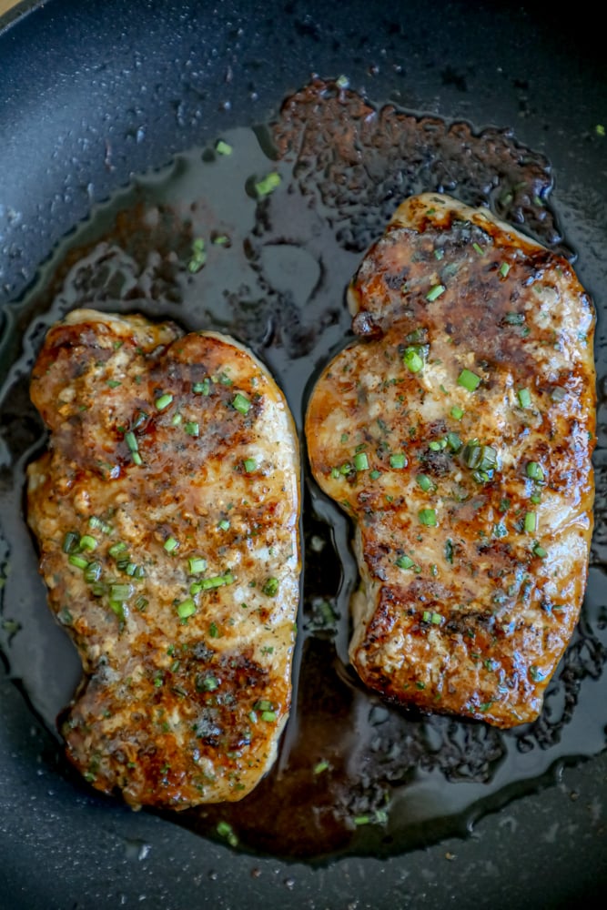 2 baked pork chops in a black pan with chives and ranch dressing seasoning on top 