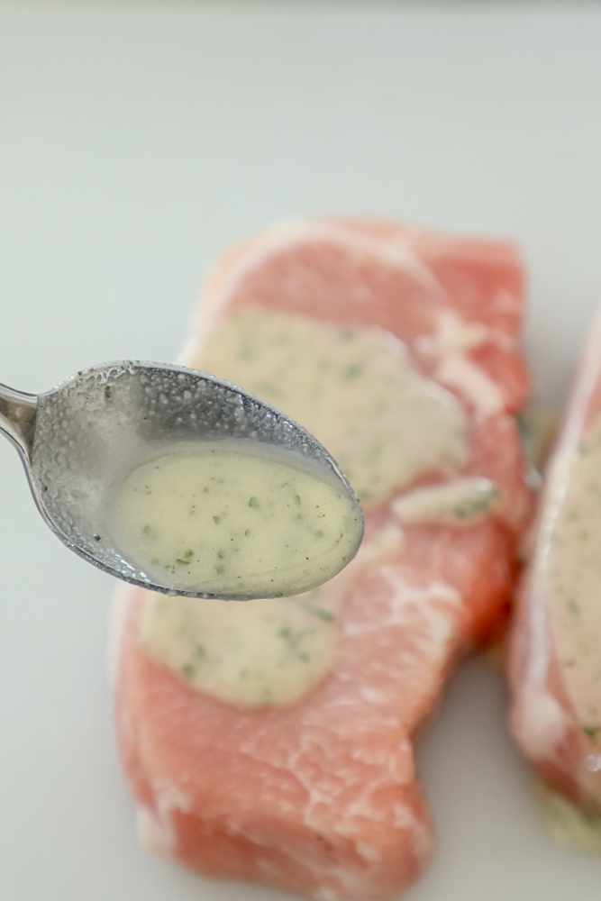 spoon pouring ranch dressing mixture on raw pork chops