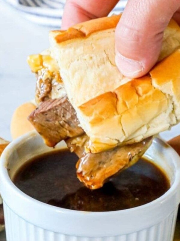 A person enjoying the best and easiest French dip au jus by dipping a sandwich into a bowl of gravy.