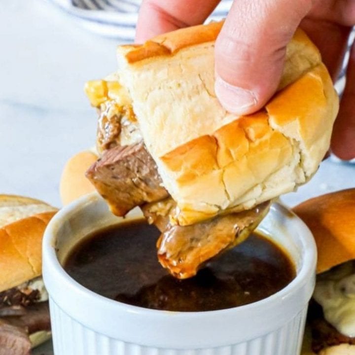 A person enjoying the best and easiest French dip au jus by dipping a sandwich into a bowl of gravy.