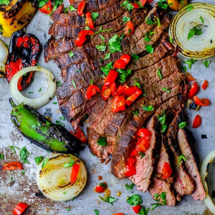 The Best Grilled Carne Asada Recipe Ever featuring a steak cooked with peppers and onions on a baking sheet.