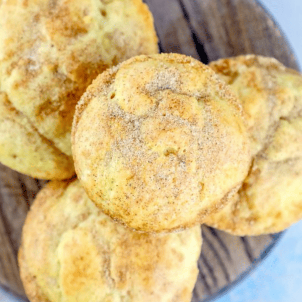 A close-up of Sour cream snickerdoodle mini muffins dusted with cinnamon-sugar on a wooden surface.