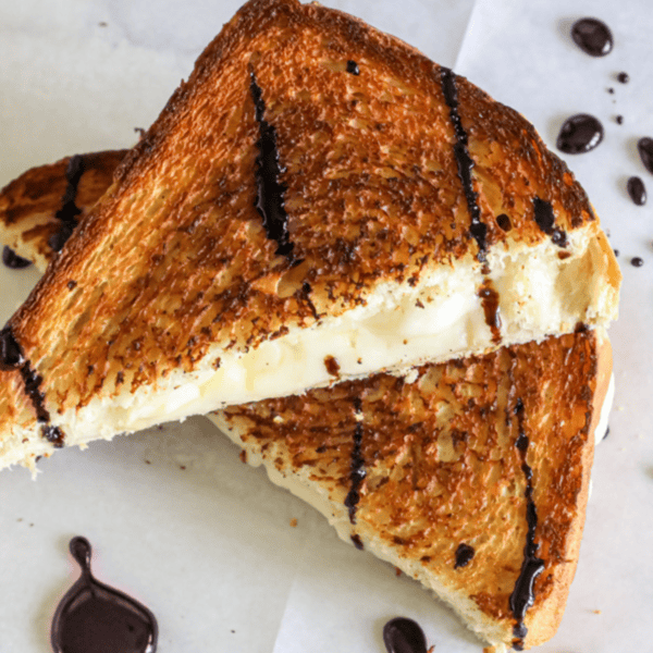 A Wine Grilled Cheese, cut diagonally and topped with dark drizzles of wine sauce, placed on parchment paper.