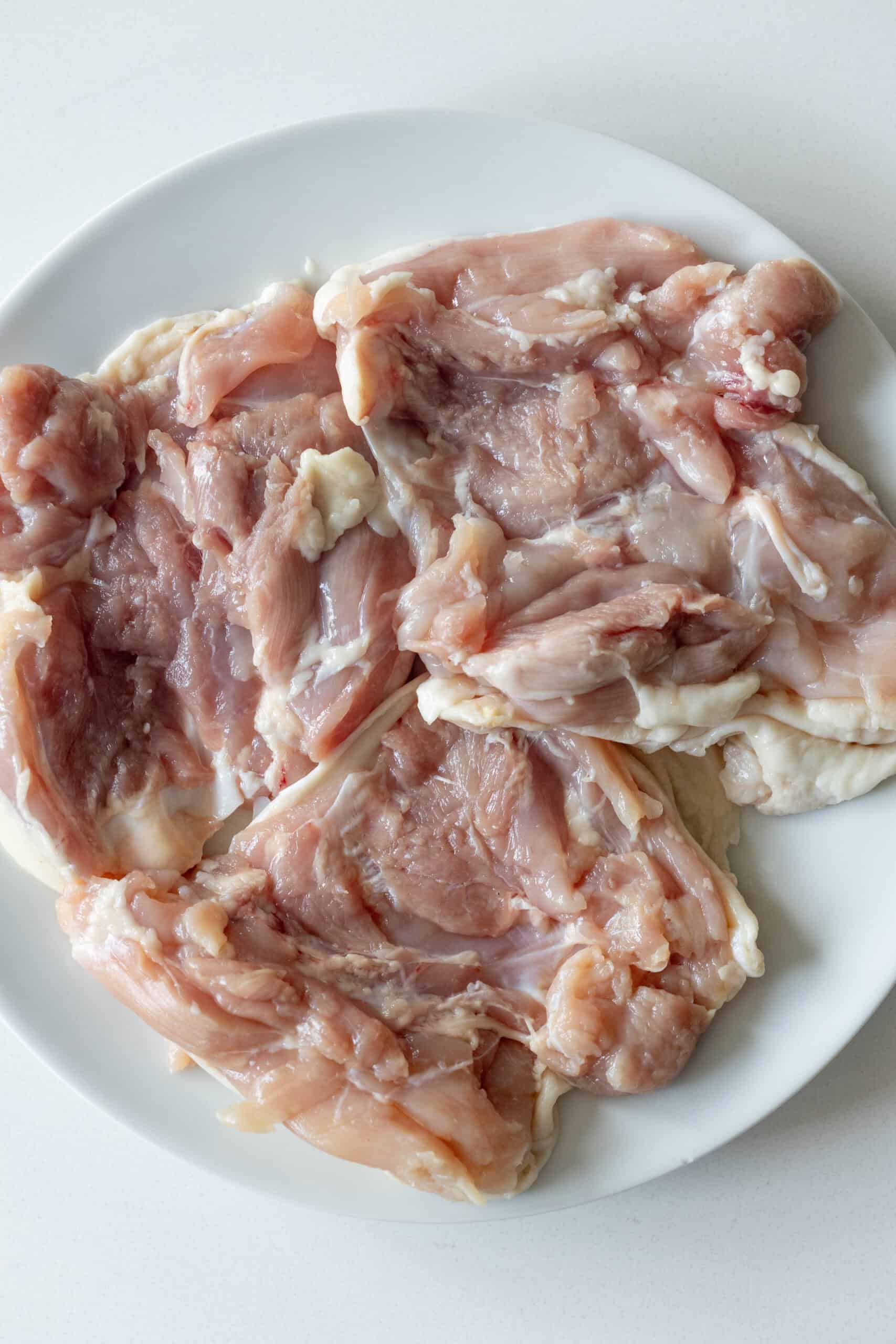 Raw, boneless, skinless chicken thighs arranged on a white plate—perfect for making pan fried chicken thighs or Keto Fried Chicken Thighs.