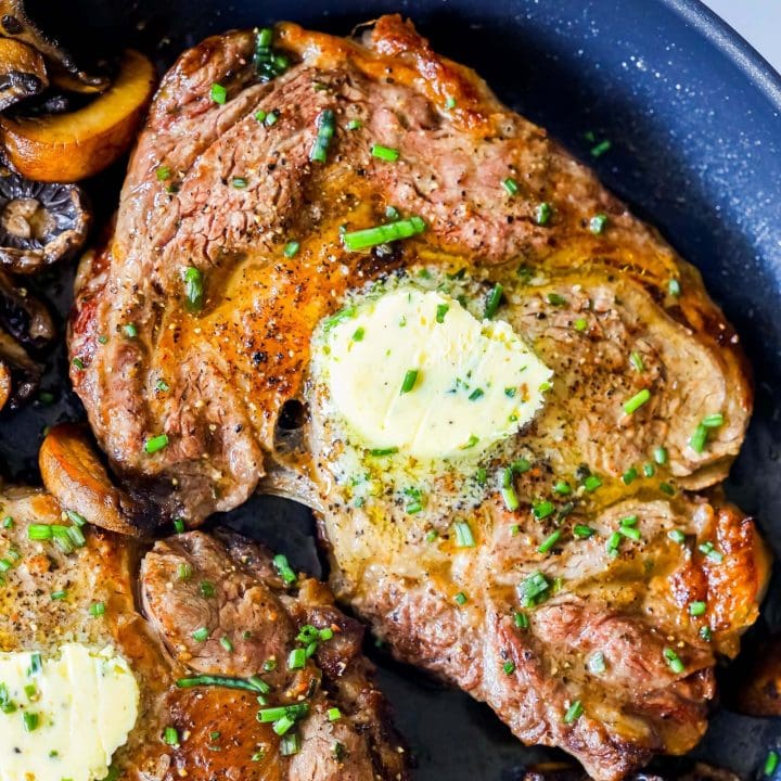 picture of ribeye steak in a pan with mushrooms and a pat of butter on top