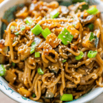 A bowl of creamy tahini noodles topped with sesame seeds, sliced green onions, and stir-fried vegetables—a delicious take on the classic tahini noodles recipe.