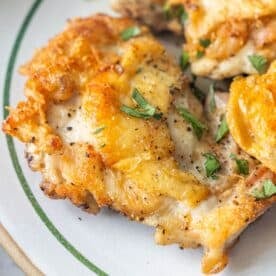 Close-up of pan fried chicken thighs with crispy golden skin, seasoned with black pepper and garnished with chopped fresh herbs on a white plate—a delicious keto fried chicken recipe.