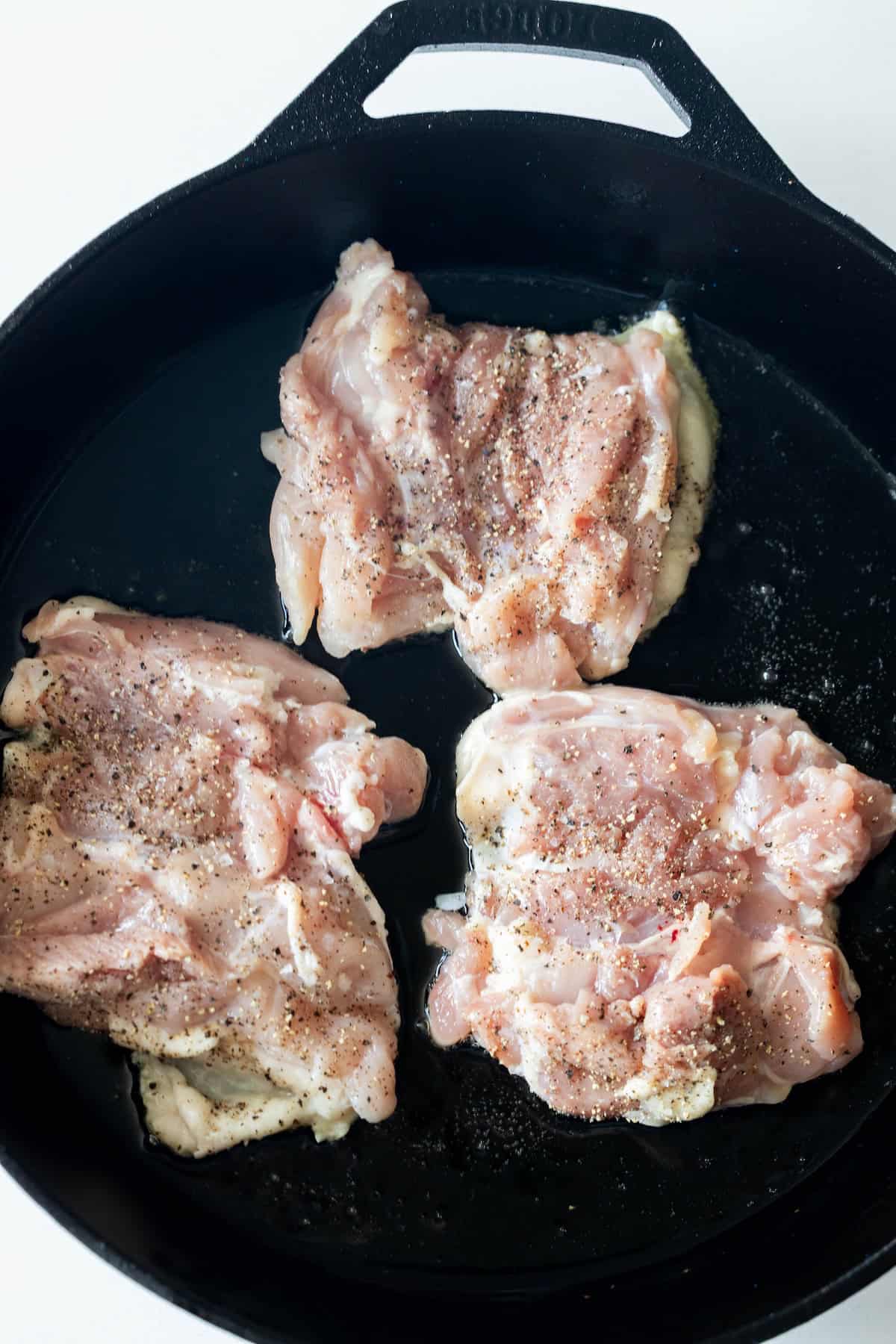 Three raw, seasoned chicken thighs are placed in a black cast iron skillet, ready to become delicious keto chicken thighs fried in butter—perfect for anyone seeking a simple keto fried chicken recipe.