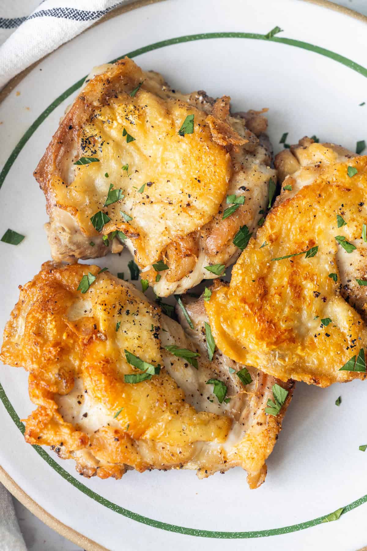 Three pieces of Keto Fried Chicken Thighs with golden, crispy skin are garnished with chopped parsley and served on a white plate with green trim. Perfect for those craving a classic keto fried chicken recipe.
