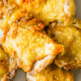 Close-up of several pieces of crispy Keto Fried Chicken Thighs with golden brown skin, pan-fried in butter, on a white surface.