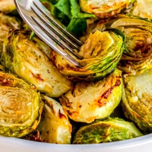 Roasted brussels sprouts in a white bowl with a fork, keto air fryer recipe.