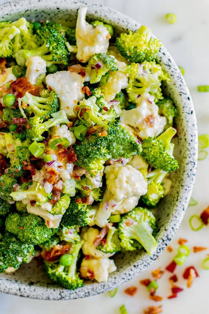creamy dressed broccoli and cauliflower in a bowl with diced bacon and onions