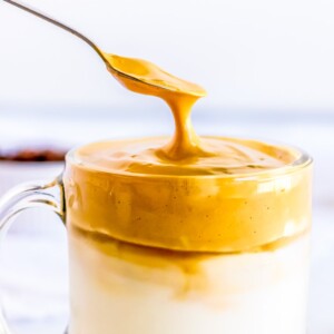 A spoon is being used to drizzle peanut butter on a cup of milk in an Easy Keto Dalgona Coffee Recipe.