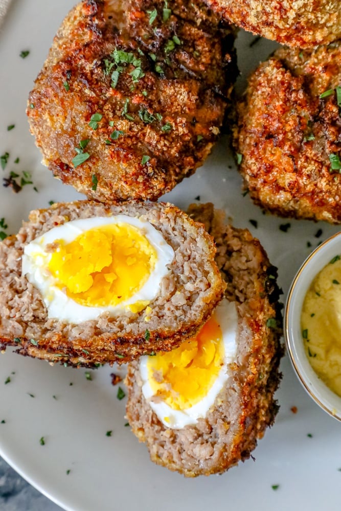 scotch eggs with keto pork rind crust cut in half on a white plate