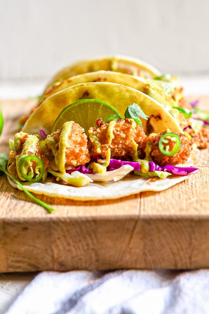 picture of fried chicken tacos in a line on a cutting board with limes on top 