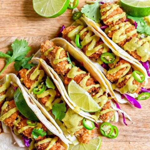 Four pan fried chicken tacos with lime and cilantro on a wooden cutting board.