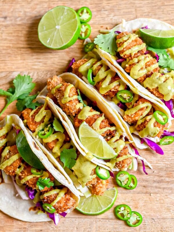 Four pan fried chicken tacos with lime and cilantro on a wooden cutting board.